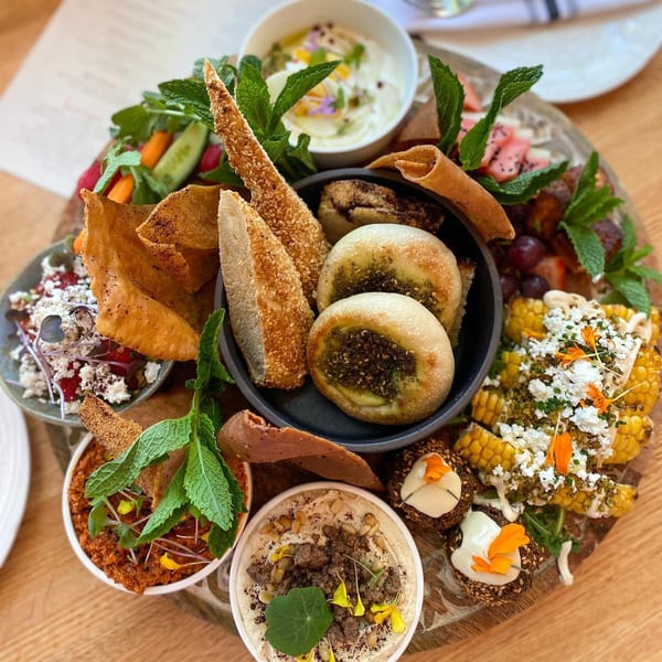 A large wooden platter filled with various Middle Eastern dishes, including dips, breads, and salads.