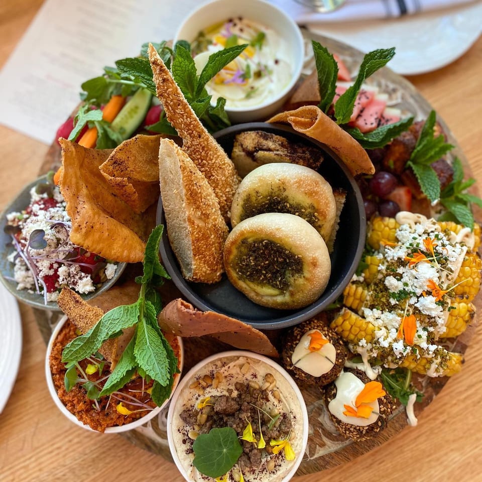 A large wooden platter filled with various Middle Eastern dishes, including dips, breads, and salads.