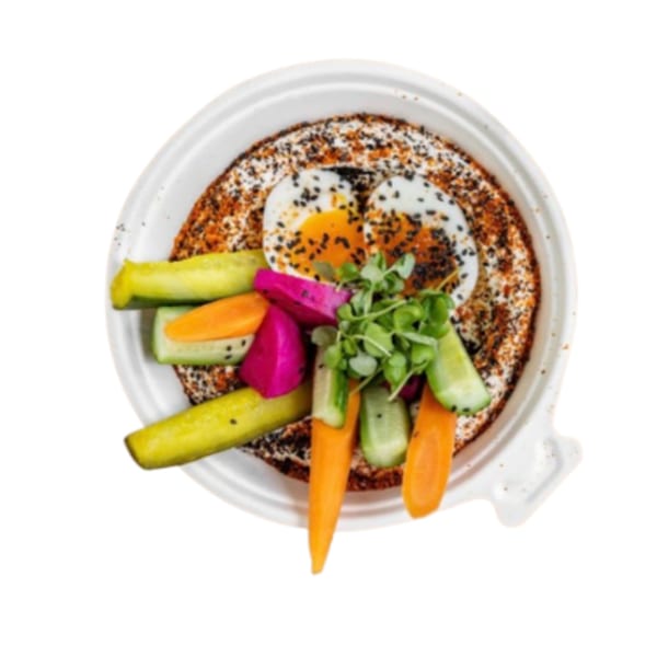 Middle-Eastern dish with two fried eggs, pickled vegetables, and microgreens in a white bowl.